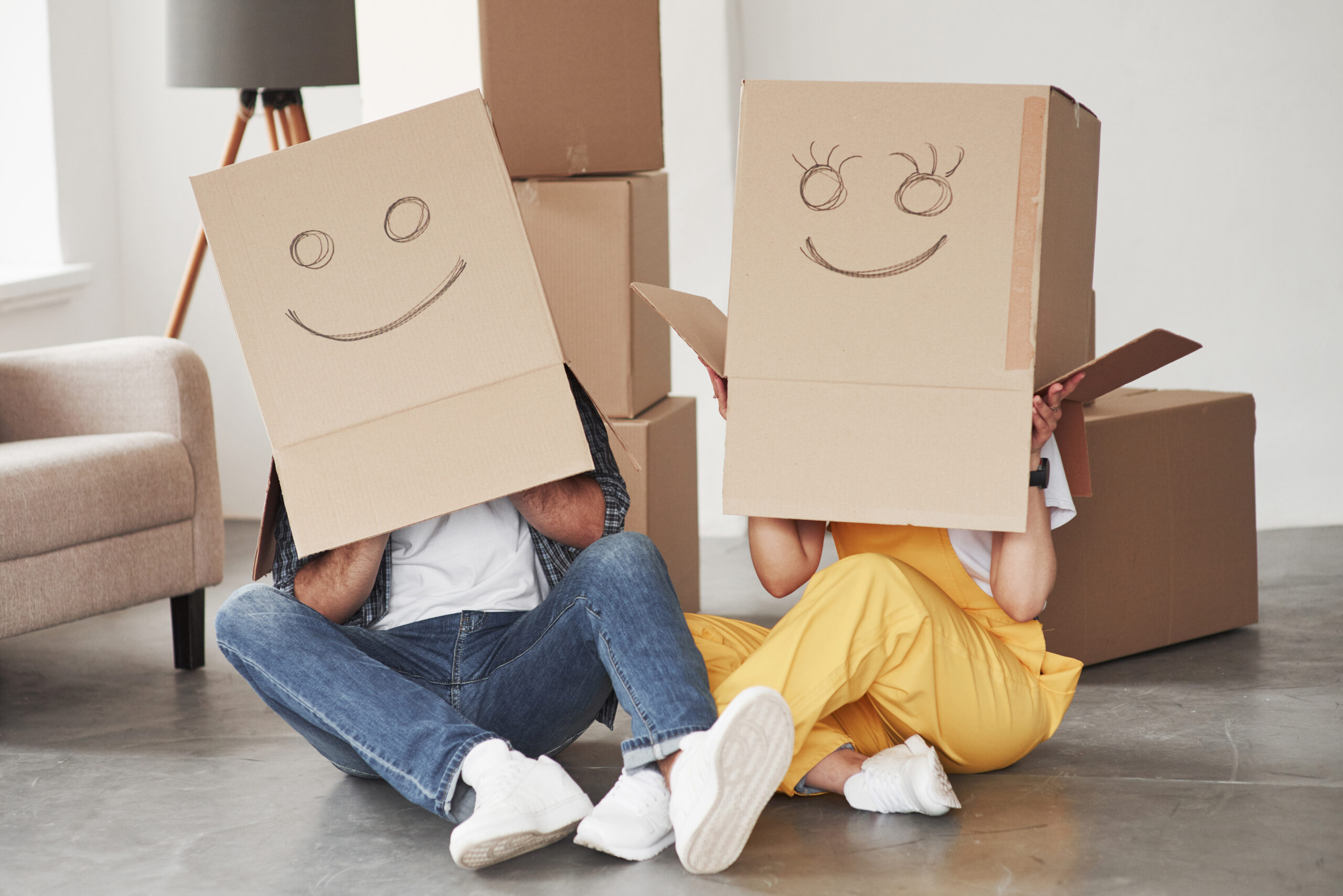 Cute smiles on boxes that is on the heads. Happy couple together in their new house. Conception of moving