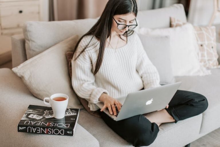 A person is sitting on a sofa, using her laptop