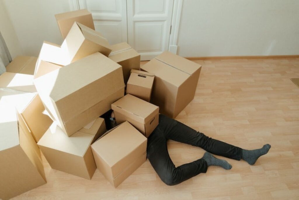 A man lying under a pile of cardboard boxes