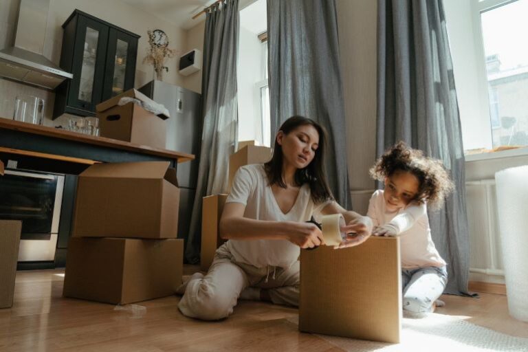 A woman and a gild are closing a moving box with tape. Getting help with packing is one of the top tips and tricks for moving across the country.