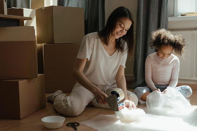 Mom and daughter sitting on the floor, wrapping items into bubble wrap and packing for a move