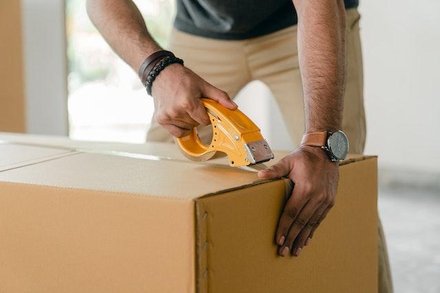 A man sealing a cardboard box with tape