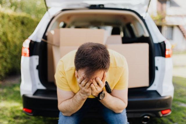 A man covering his face with his hands near a car trunk