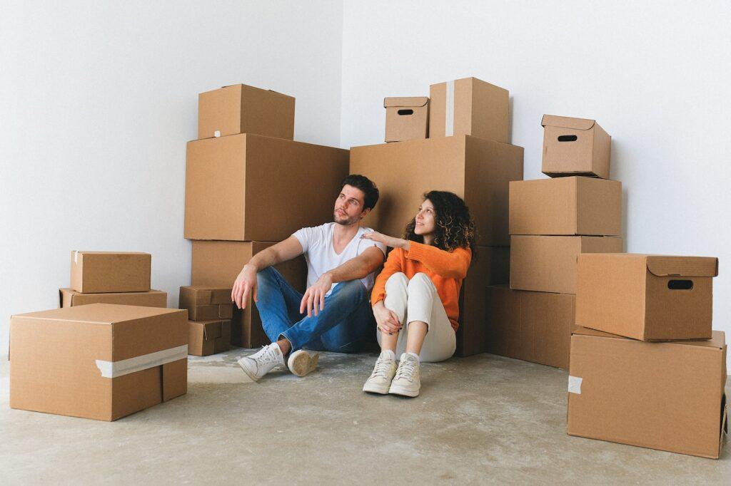 A couple sitting on the floor next to their moving boxes.