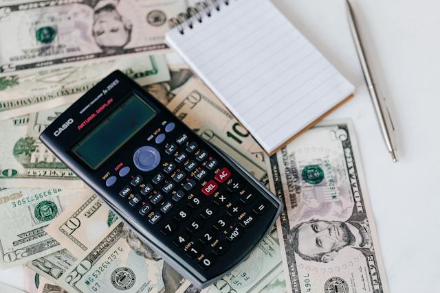 A calculator, a notepad, and a pen on a pile of money.