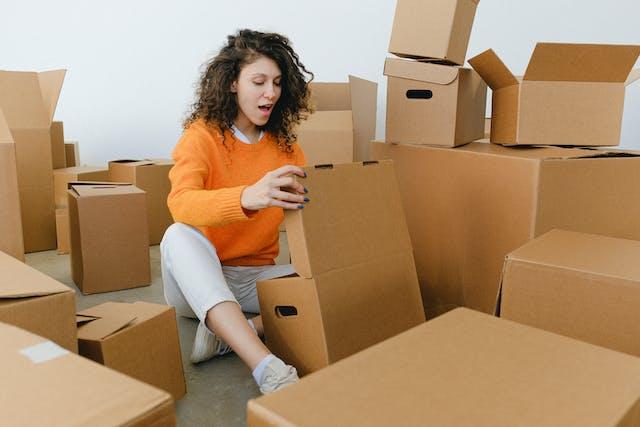 An individual surrounded by cardboard boxes looking surprised, possibly during a moving process.