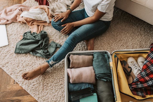 A person sitting on the floor next to an open suitcase, carefully packing clothes for moving